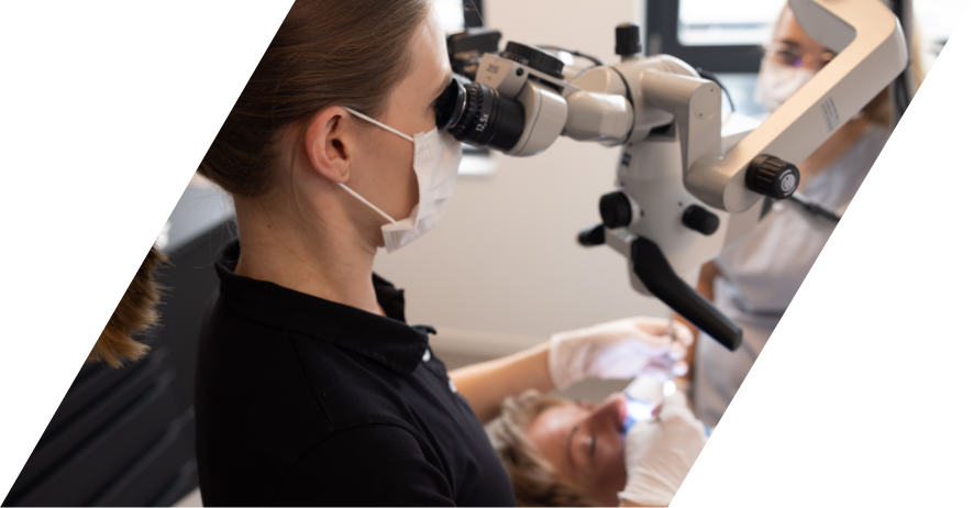 Zahnärztin Dr. Miriam Fischer betrachtet die Zähne einer Patientin durch ein Mikroskop